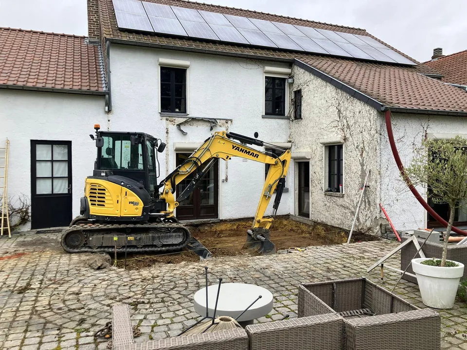 Mini-pelle jaune au terrassement devant la façade
