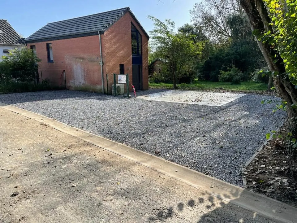 Zone empierrée avec bordure en béton devant un bâtiment en briques