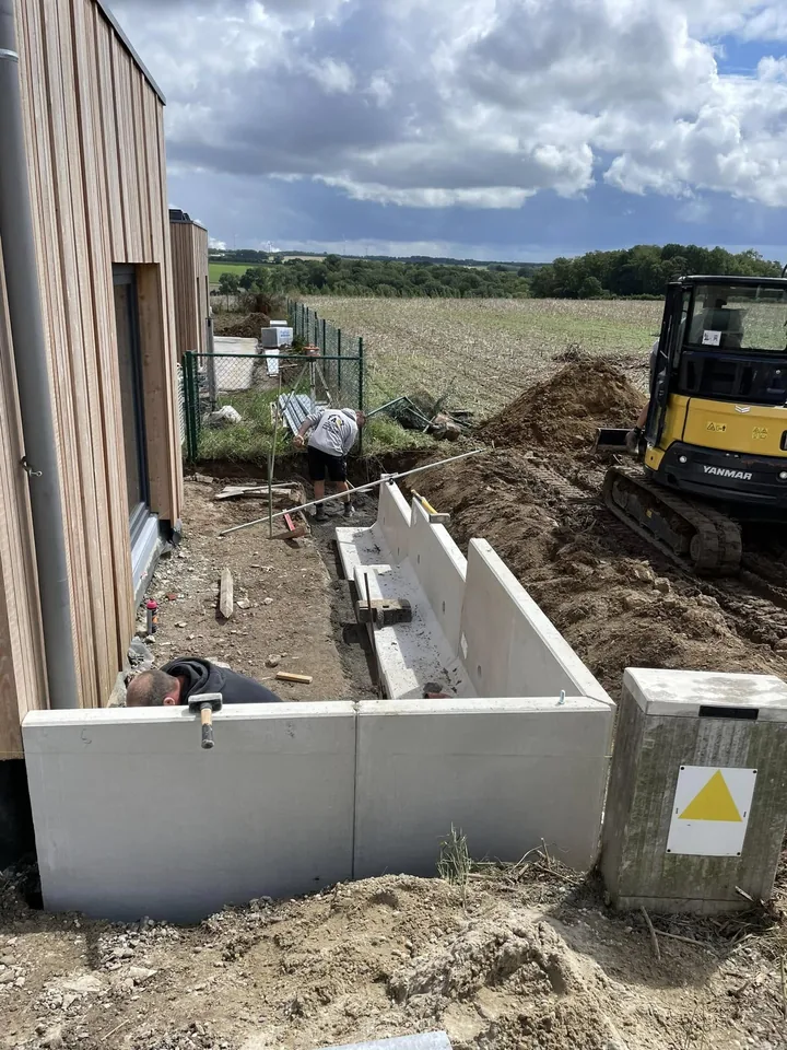 Éléments en L en béton posés, mini-pelle jaune au fond