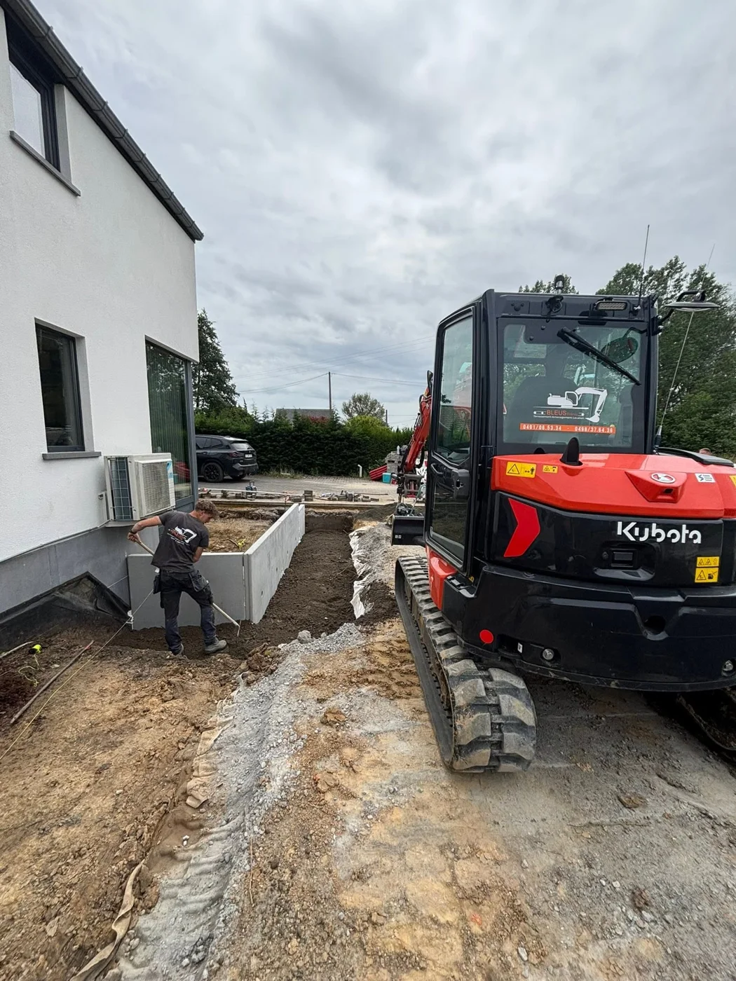 Mini-pelle vue de dos sur un chantier d'aménagement, devant une maison